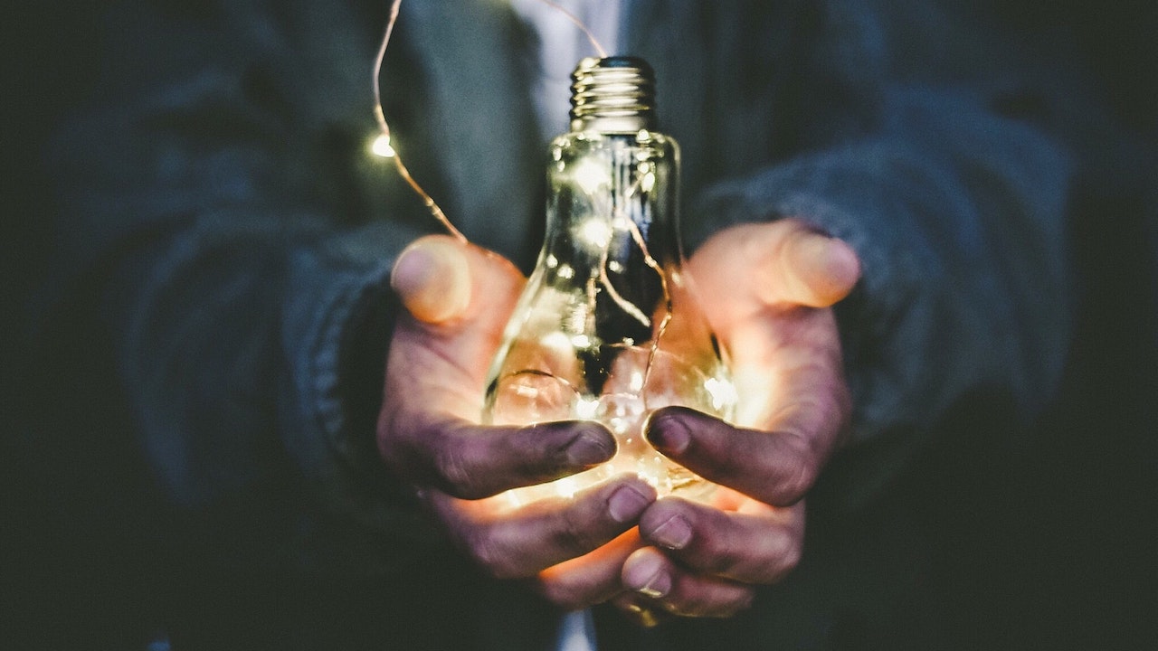 A pair of hands holding a lightbulb filled with fairy lights