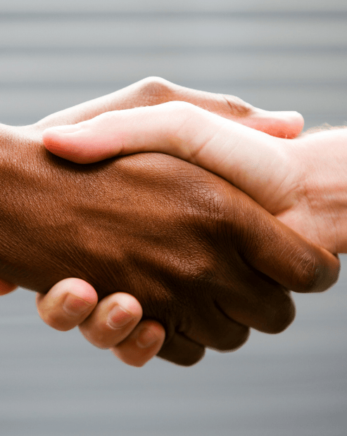 Small hero image promoting the Art of Negotiation Workshop. A tight close-up of a firm handshake between two people with different skin tones. The hands are centred against a neutral, blurred grey background with subtle horizontal lines. The image represents agreement, partnership, and the successful conclusion of a professional or personal deal.
