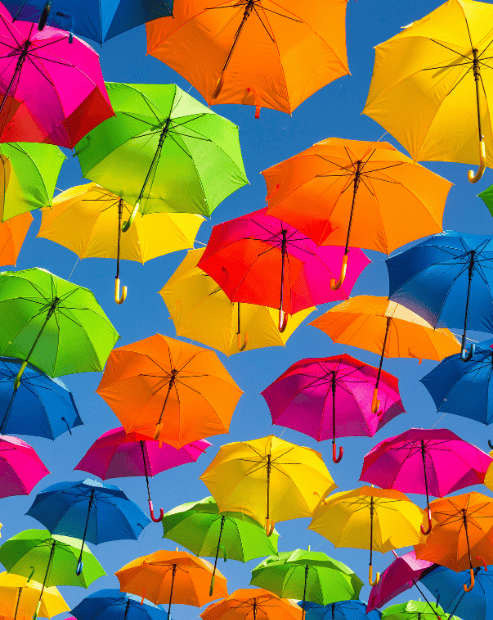 Small hero image for creatives guide to super insurance workshop. A low-angle perspective looking up at a dense canopy of vibrant, open umbrellas in shades of pink, yellow, blue, and orange against a clear, bright blue sky.
