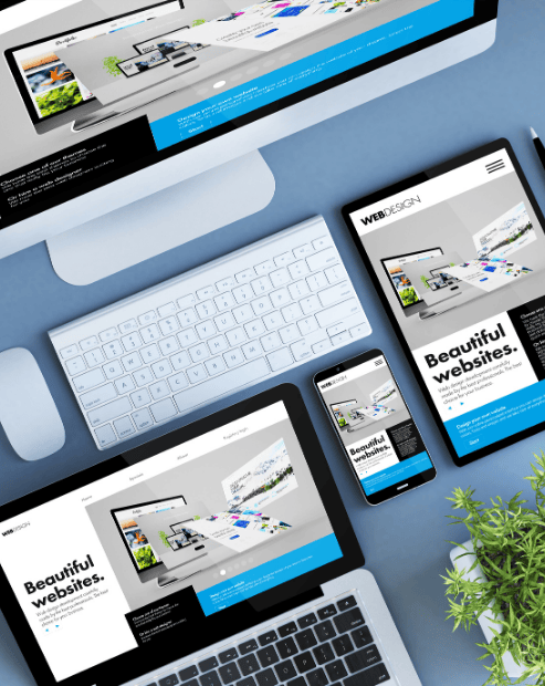 Small hero image promoting the Creative's Guide to Websites Workshop. A high-angle view of a modern blue workspace displaying a website design across multiple synchronized devices, including a desktop monitor, laptop, tablet, and smartphone. The screens all feature the headline "Beautiful websites." The desk also contains a white keyboard, mouse, a pen, two USB drives, and a small green plant, representing a comprehensive approach to responsive web design.