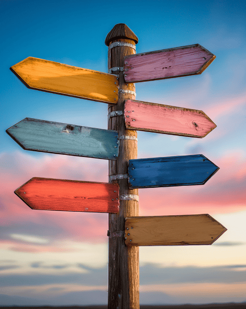 A rustic wooden signpost with multiple colorful, blank arrows pointing in different directions against a soft sunset sky with blue and orange hues. The image represents the diversify your creative income workshop.