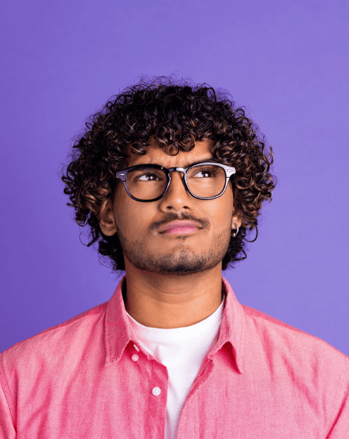 Small gero image for the pricing for creatives whats it worth workshops. A man with curly hair and glasses, wearing a pink collared shirt over a white t-shirt, looking upward with a thoughtful and sceptical expression against a solid purple background.